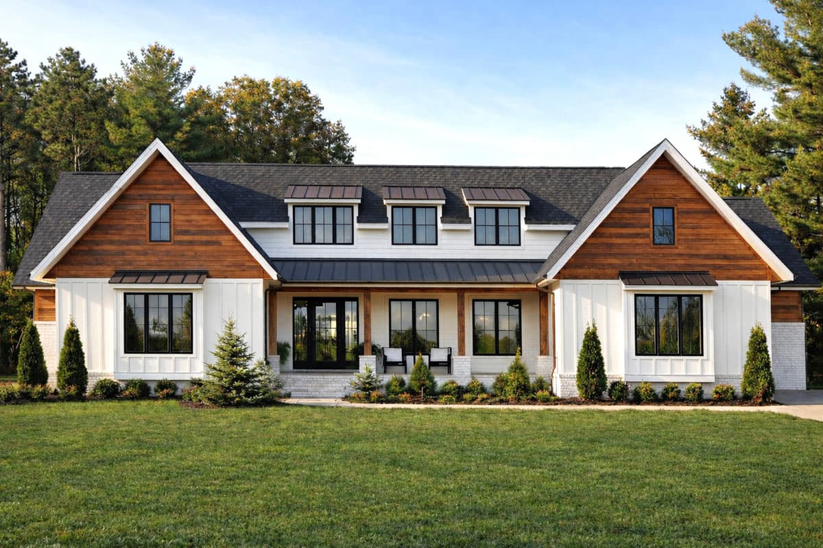 A modern farmhouse with a dark roof, white siding, and wood accents. The house has several black-framed windows and a green lawn.
