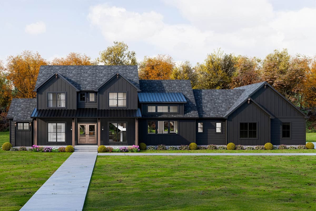 A modern, black-sided modern farmhouse style house with a long driveway is set against a backdrop of fall foliage and a bright blue sky.
