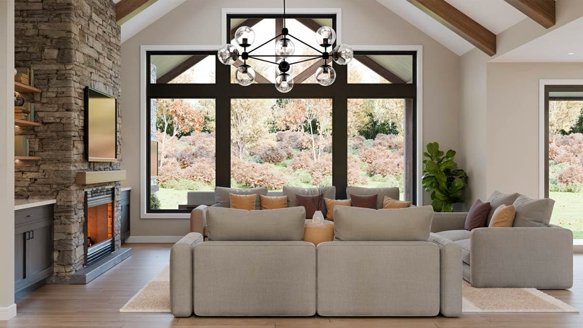 A modern living room with a stone fireplace, large windows overlooking a wooded area, and a large sectional sofa with colorful pillows.