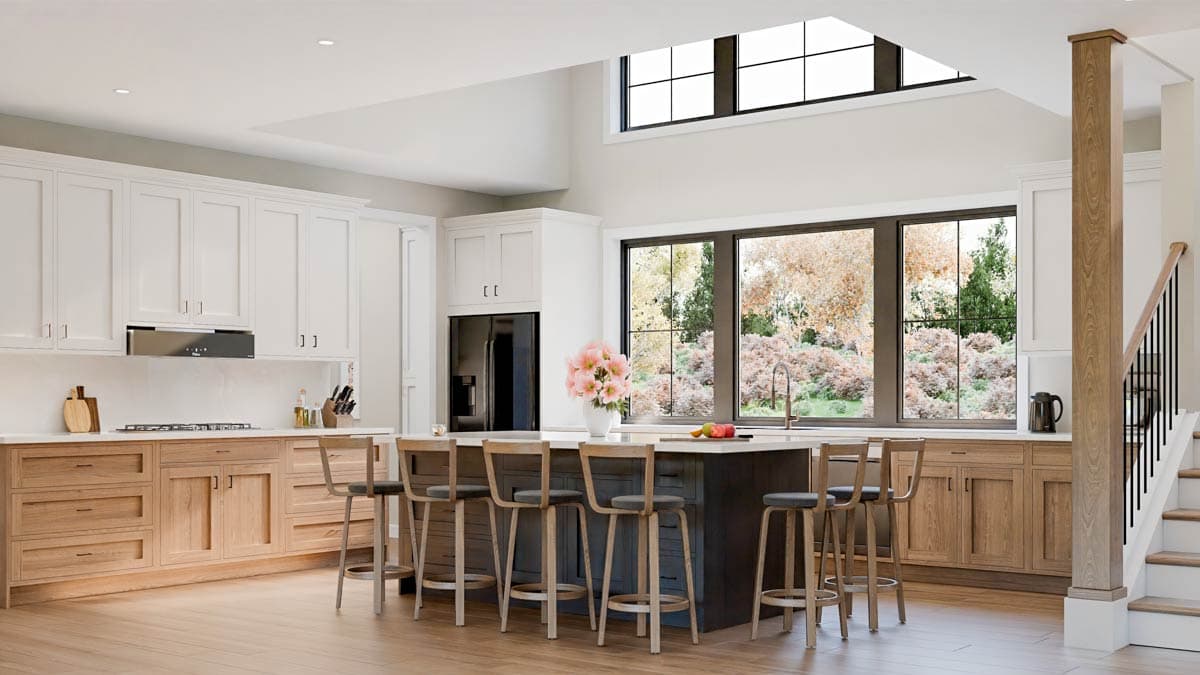 A modern kitchen with a large island and bar stools, lots of natural light from large windows, and a staircase leading upstairs.