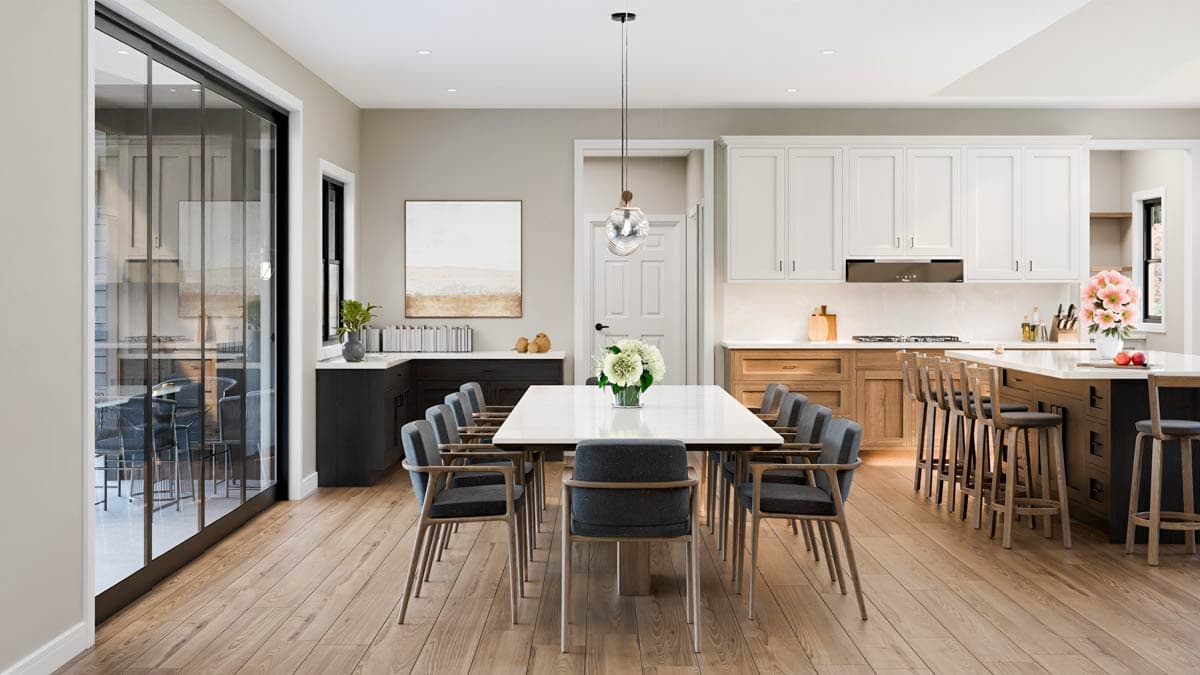 A modern dining room with a long white table set for a meal, surrounded by gray chairs. A kitchen with a large island and bar stools is visible.