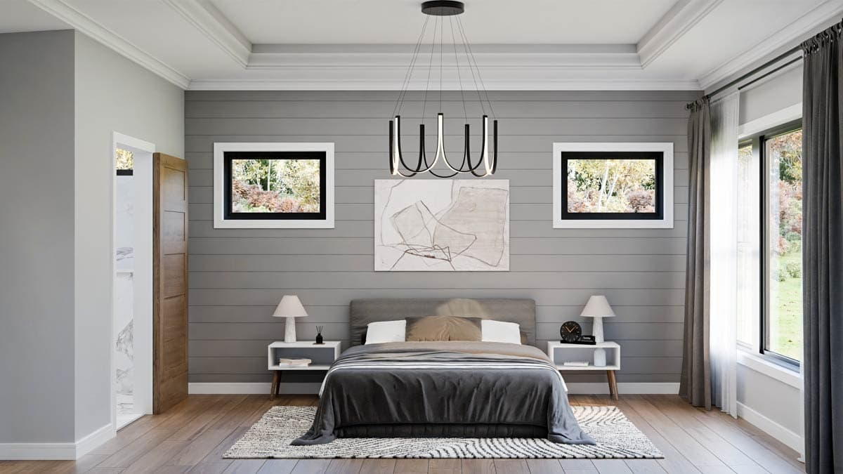A modern bedroom with gray walls, wood floors, and a large bed. Two windows offer views of trees. A unique chandelier hangs above the bed.