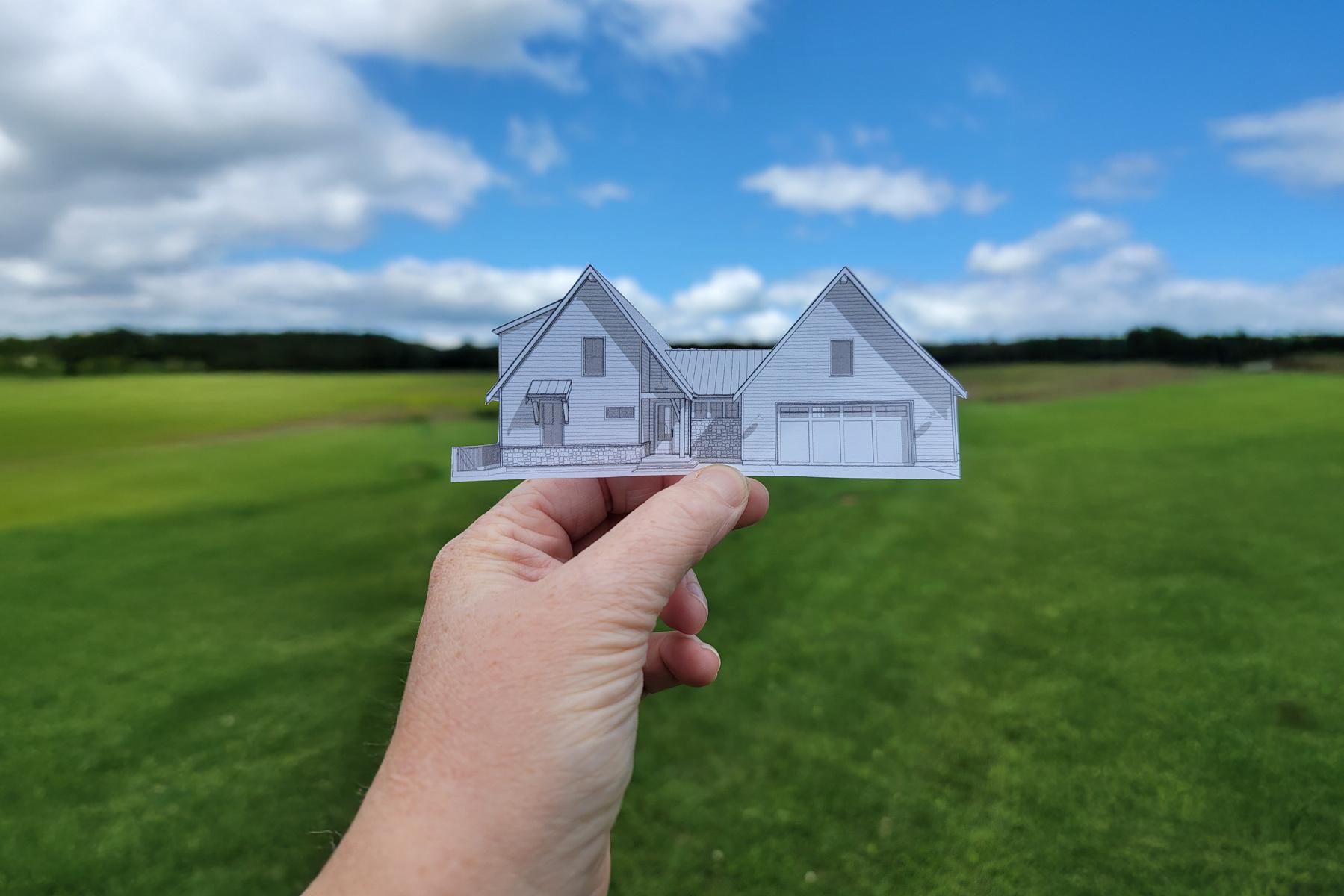 Hand holding a paper house plan cutout of Architectural Designs plan 270072AF, representing the Facebook Group Exclusive Client Community for customers building their homes